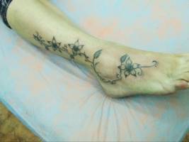 Tatuaje de una enredadera con flores por el pie de una chica