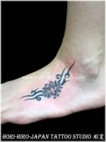Tatuaje de una pequeña flor con un tribal en el pie