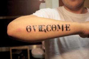 Tatuaje de la frase Overcome en el antebrazo