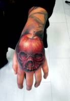 Tatuaje a color en la mano de una calavera con forma de manzana 