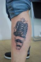 Tatuaje de un micrófono rodeado por una cinta