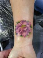 Tatuaje de una flor de loto a color en la muñeca